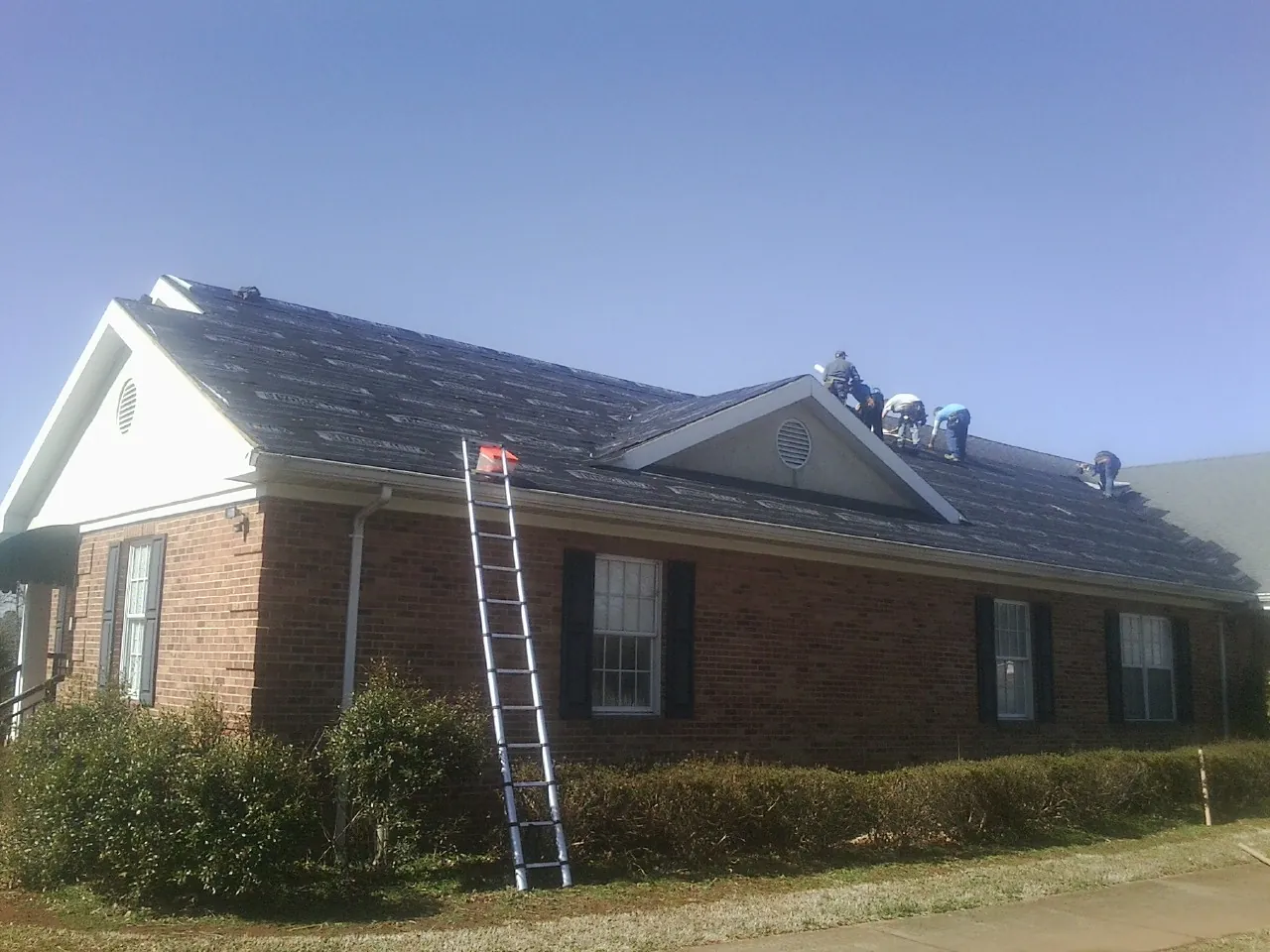 Crew tearing shingles off a brick ranch roof with a ladder set — Emergency Roof Repair work by our crew in Grass Valley