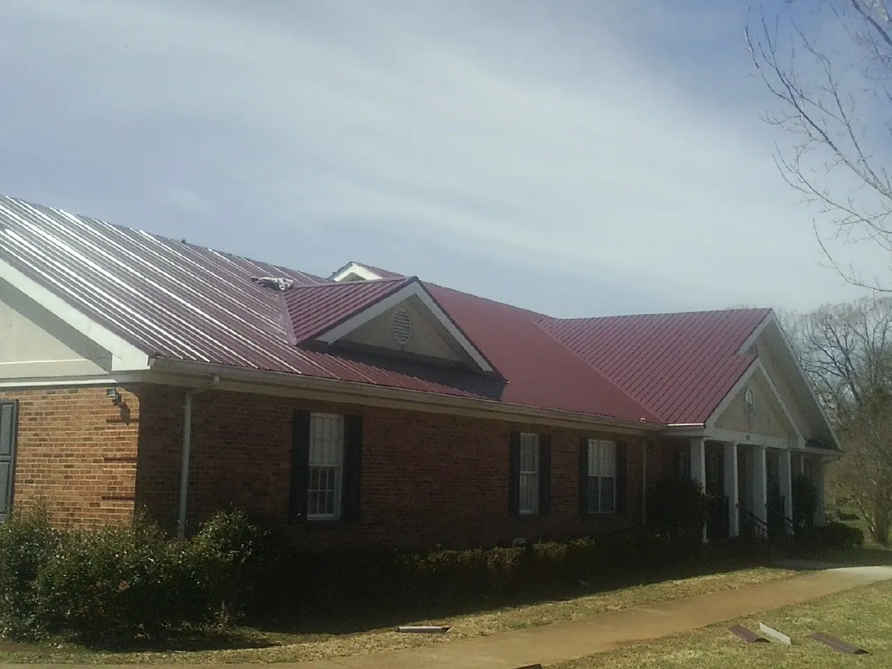 Red metal roof with gabled entries on a long brick building, from a Hail Damage Roof Repair job in Grass Valley
