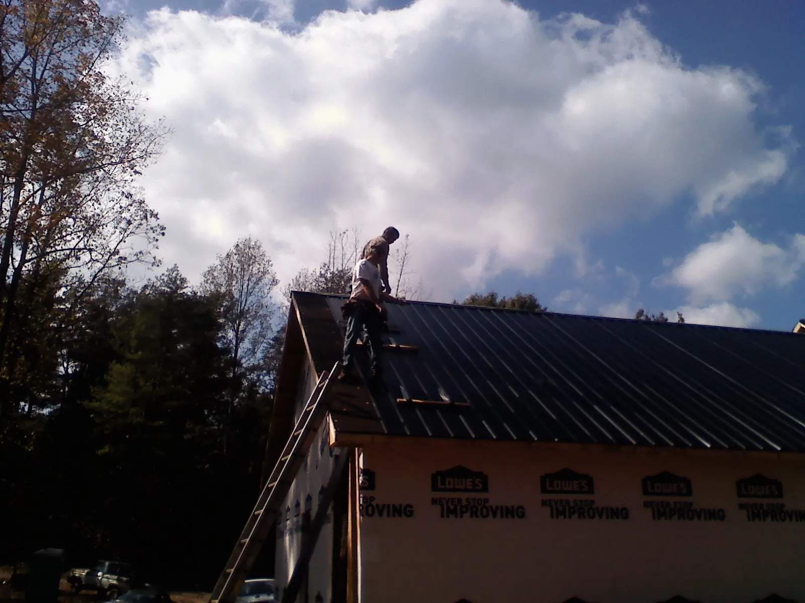 Roofer fastening dark metal panels high against a cloudy sky, from a Roof Inspection job in Grass Valley